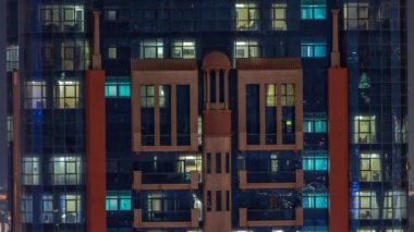 Aydınlatılmış çalışma odası saatleriyle apartman penceresi ön cephesinin gece hava görüntüsü.