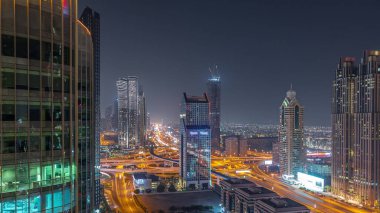 Dubai şehrinin gökyüzü panoramik manzaralı metro ve arabaları şehrin en işlek karayolu gece zaman çizgisinde ilerliyor. Parlak pencereli gökdelenlerle çevrili kavşak