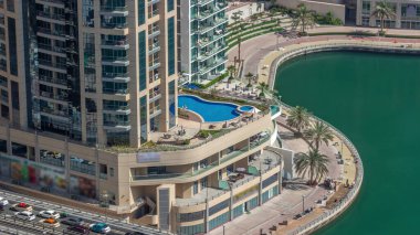 Dubai Marina rıhtımı ve yüzme havuzu zaman ayarlı şehir turu. Kanallar boyunca gökdelenlerin havadan görüntüsü. İnşaat işçileri fayans yolu yapıyor.