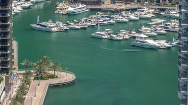 Limanda yüzen yatların hava görüntüsü zaman ayarlı. Dubai Marina 'da limana yakın park edilmiş beyaz tekneler var. Avuç içleriyle gezinme
