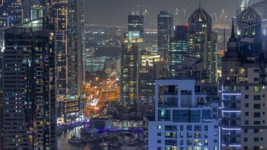 Dubai Marina ve Medya Şehri bölgelerinde modern gökdelenler ve ofis binaları gece uçuşları. Üst geçitte trafik ve şehir merkezindeki kulelerde kavşak.