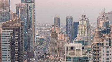 Dubai Marina ve Medya Şehri 'nin modern gökdelenleri ve ofis binaları ile hava gününden geceye geçiş zamanı. Yeşil park yakınlarındaki üst geçitte trafik ve kavşak.