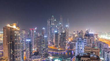 Dubai Marina hava sahasının en yüksek bloğundaki çeşitli gökdelenlerin görüntüsü tüm gece boyunca yapay kanallı. Yanıp sönen ışıkları ve yatları olan bir sürü kule. Bulutlu gökyüzü