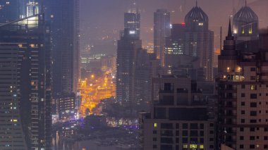 Dubai Marina ve Media City semtleri modern gökdelenler ve ofis binaları gece gündüz geçiş zamanları. Limandaki yatların yakınındaki üst geçitte trafik ve kavşak.