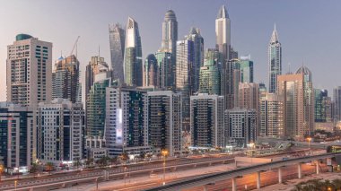 Dubai marinası gökdelenlerin en uzun bloğu günden geceye geçiş zamanı. JLT bölgesinden apartman binalarına, otellere ve otoyol yakınlarındaki iş kulelerine hava manzarası.