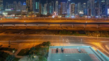 Dubai Marina gökdelenleri ve Şeyh Zayed yolu ile metro demiryolu hava akımının zaman çizelgesi. Otoparktaki arabalar. Modern kulelerin yakınındaki bir otoyolda trafik var, Birleşik Arap Emirlikleri