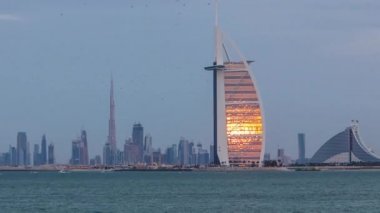Gün batımında ve gece saatlerinde Burj Al Arap oteli ile Dubai silueti.
