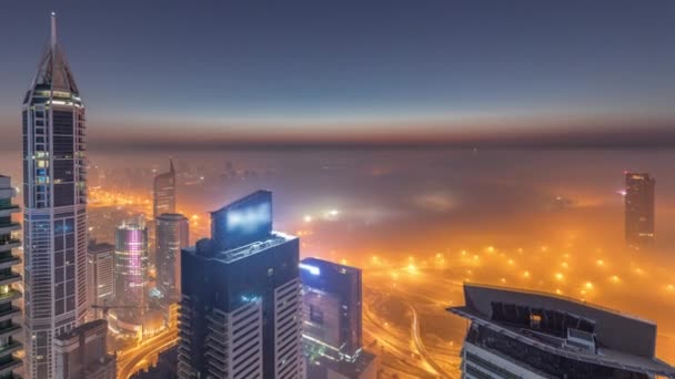Rara niebla de invierno temprano en la mañana sobre el horizonte de Dubai Marina y rascacielos iluminados por luces de la calle noche aérea al día timelapse. — Vídeo de stock