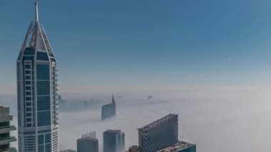 Dubai Marina silueti ve gökdelenlerin üstündeki nadir kış sisi ve çatıların zamanlaması..