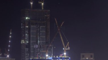 İnşaat halindeki çok katlı binalar ve gece vakti vinçler.