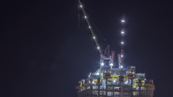 Edificio de varios pisos de altura en construcción y grúas en horario nocturno — Vídeo de stock