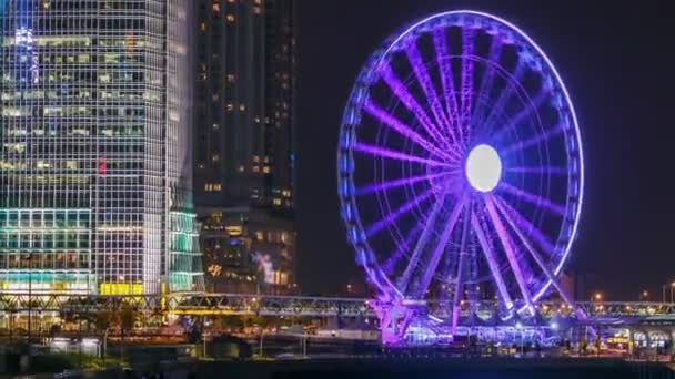 Timelapse nocturno de rascacielos y rueda de observación de Hong Kong, que es la última atracción turística de la ciudad . — Vídeos de Stock