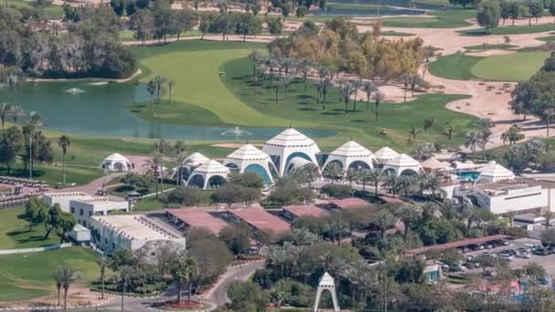 Letecký pohled na golfové hřiště se zeleným trávníkem a jezery, vilové domy za ním timelapse. — Stock video
