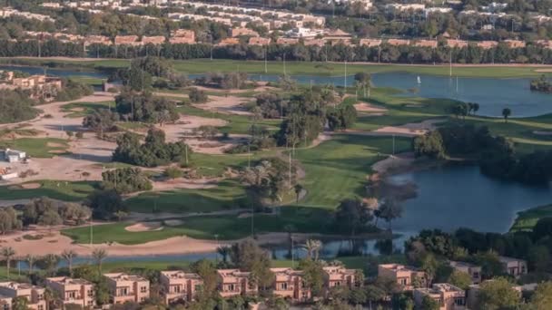 Вид с воздуха на поле для гольфа с зеленой лужайкой и озерами, виллы позади нее. — стоковое видео