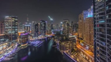 Kanal çevresindeki Dubai marina gökdelenlerine gece vakti yüzen teknelerle hava görüntüsü.
