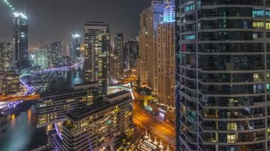 Kanal çevresindeki Dubai marina gökdelenlerine gece vakti yüzen teknelerle hava görüntüsü.