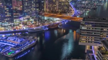 Kanal çevresindeki Dubai marina gökdelenlerine gece vakti yüzen teknelerle hava görüntüsü.