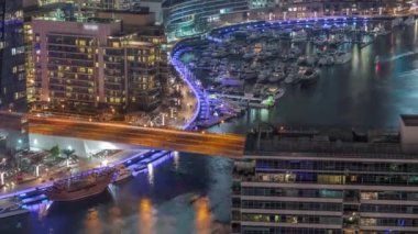 Kanal çevresindeki Dubai marina gökdelenlerine gece vakti yüzen teknelerle hava görüntüsü.
