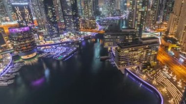 Kanal çevresindeki Dubai marina gökdelenlerine gece vakti yüzen teknelerle hava görüntüsü.
