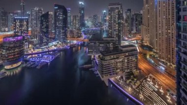Kanal çevresindeki Dubai marina gökdelenlerine gece vakti yüzen teknelerle hava görüntüsü.
