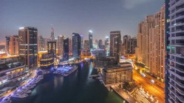 Kanal etrafındaki Dubai marina gökdelenlerine gece gündüz yüzen teknelerle hava görüntüsü.