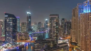 Kanal çevresindeki Dubai marina gökdelenlerine gece vakti yüzen teknelerle hava görüntüsü.