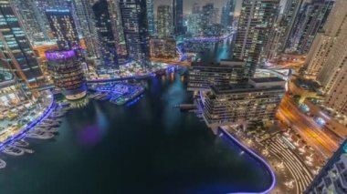 Kanal çevresindeki Dubai marina gökdelenlerine gece vakti yüzen teknelerle hava görüntüsü.
