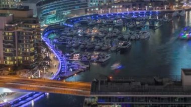 Kanal çevresindeki Dubai marina gökdelenlerine gece vakti yüzen teknelerle hava görüntüsü.