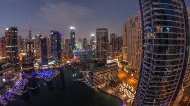Kanal etrafındaki Dubai marina gökdelenlerine gece gündüz yüzen teknelerle hava görüntüsü.