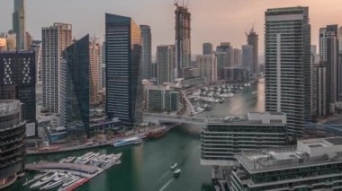 Kanal çevresindeki Dubai marina gökdelenlerine gün be gece yüzen teknelerle hava görüntüsü