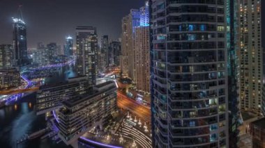 Kanal çevresindeki Dubai marina gökdelenlerine gece vakti yüzen teknelerle hava görüntüsü.