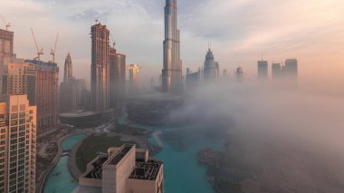 Dubai şehrinin hava panoramik görüntüsü sabahın erken saatlerinde sis zamanlarında. Gökdelenler ve gökdelenlerle dolu fütüristik şehir siluetinde gün doğumu. Güneş cam yüzeyden yansıyor