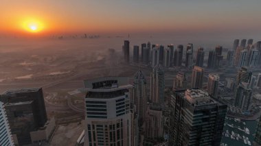 Dubai Marina Panoraması 'nda güneş doğarken JLT gökdelenleri ve golf sahası, Dubai, Birleşik Arap Emirlikleri. Yukarıdan hava manzarası sisli bir sabah. Turuncu gökyüzü ile şehir silueti