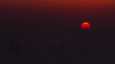 Sabah Dubai ufuk çizgisinde gün doğumu yakın görüntüsü, Dubai marinası zaman çizelgesinden gökyüzü görüntüsü. Turuncu gökyüzündeki büyük güneş gökdelenlerin etrafındaki sislerin üzerinde yükseliyor. Birleşik Arap Emirlikleri