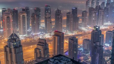 Şeyh Zayed Yolu yakınlarındaki JLT gökdelenleri ve marina kuleleri gece gündüz geçiş zamanı. Aydınlatılmış konut binaları ve villalarla ufuk çizgisi. Güneş doğmadan önce sisli bir sabah