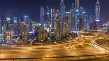 Dubai Marina 'nın gökdelenleri tüm gece boyunca ışıklandırılmış en yüksek konut binaları ve ışıkları kapalı. JLT bölgesinden hava görüntüsü. Otoyolda trafik vardı.