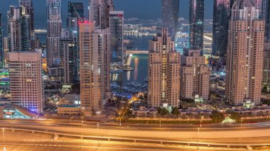 Dubai Marina 'nın gökdelenleri gece gündüz geçiş zamanlarında en yüksek konut binalarıyla aydınlandı. Güneş doğmadan önce JLT bölgesinin havadan görüntüsü. Yatlar suda yüzüyor.