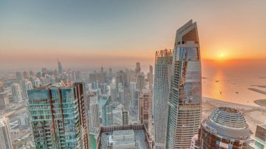 Dubai Marina 'nın gün batımı manzarası kıyı şeridi boyunca gökdelenlerle çevrili yapay bir kanal gösteriyor. Modern kulelerin üzerinde turuncu gökyüzü. Dubai, BAE