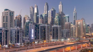 Dubai marinası gökdelenlerin en uzun bloğu günden geceye geçiş zamanı. JLT bölgesinden apartman binalarına, otellere ve otoyol yakınlarındaki iş kulelerine hava manzarası.