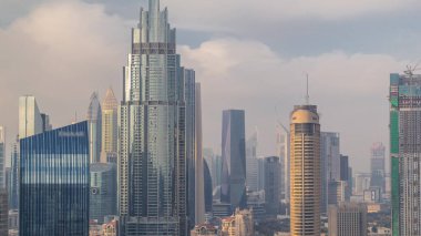 Dubai şehir merkezinden yükselen gökdelenler, alışveriş merkezi ve finans merkezi modern binalarla çevrili. Gökyüzü bulutlu.