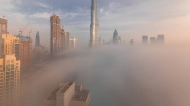 Dubai şehrinin hava panoramik görüntüsü sabahın erken saatlerinde sis zamanlarında. Gökdelenler ve gökdelenlerle dolu fütüristik şehir siluetinde gün doğumu. Güneş cam yüzeyden yansıyor