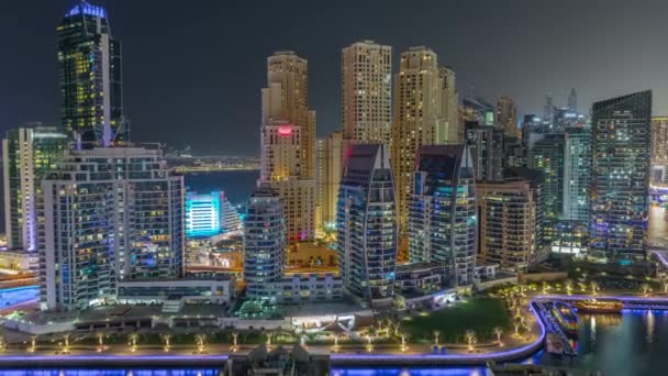 Dubai Marina con varios barcos aparcados cerca del paseo marítimo y rascacielos alrededor del canal de la noche aérea timelapse. — Vídeos de Stock