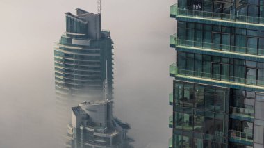 Dubai Marina ufuk çizgisi üzerinde nadir bulunan kış sisi ve hava saatleri üzerinde cam gökdelenlerle kaplı kuleler. Üst görünüm bulutların üstünde. Dubai, BAE