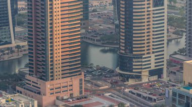 Dubai lüks konut bölgesinde hafif araçlar için park yeri, yukarıdan hava manzaralı. Akşam turuncu ışıklı JLT gökdelenleri