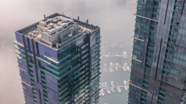 Modern gökdelenler, hava zaman çizelgeleri ve Dubai Marina 'nın sabah puslu su iskelesi, Birleşik Arap Emirlikleri. Yatlar ve kayıklar cam kuleler arasında