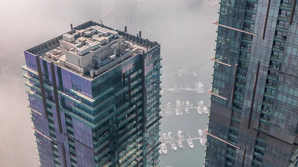 Modern gökdelenler, hava zaman çizelgeleri ve Dubai Marina 'nın sabah puslu su iskelesi, Birleşik Arap Emirlikleri. Yatlar ve kayıklar cam kuleler arasında