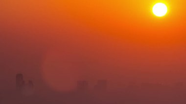 Sabah Dubai ufuk çizgisinde gün doğumu yakın görüntüsü, Dubai marinası zaman çizelgesinden gökyüzü görüntüsü. Turuncu gökyüzündeki büyük güneş gökdelenlerin etrafındaki sislerin üzerinde yükseliyor. Birleşik Arap Emirlikleri