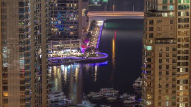 Dubai Marina 'daki gezinti güvertesi ve kanalı. Gece vakti, Birleşik Arap Emirlikleri civarında aydınlık lüks gökdelenleri var. Yatlar ve tekneler yukarıdan kanala bakıyor.