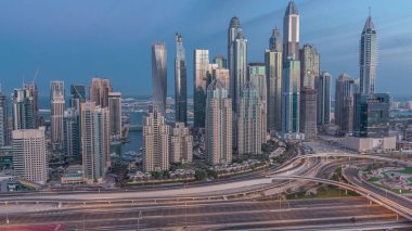 Dubai Marina karayolu kavşağı spagetti kavşağı gece gündüz geçiş zamanı. Arka planda en uzun gökdelenler aydınlatılıyor. Güneş doğmadan önce JLT bölgesinden hava üst görünümü