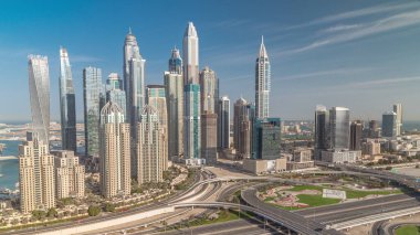 Dubai Marina karayolu kavşağı spagetti kavşağı zaman dilimi. Arka plandaki en uzun gökdelenler. JLT bölgesinden sabah hava görüntüsü. Bulutlu gökyüzü